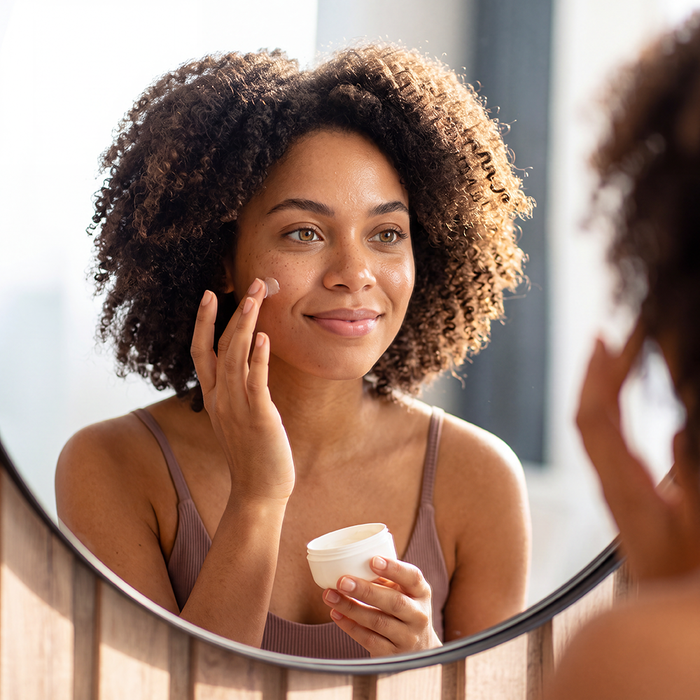 Femme devant un miroir qui passe une crème sur la joue